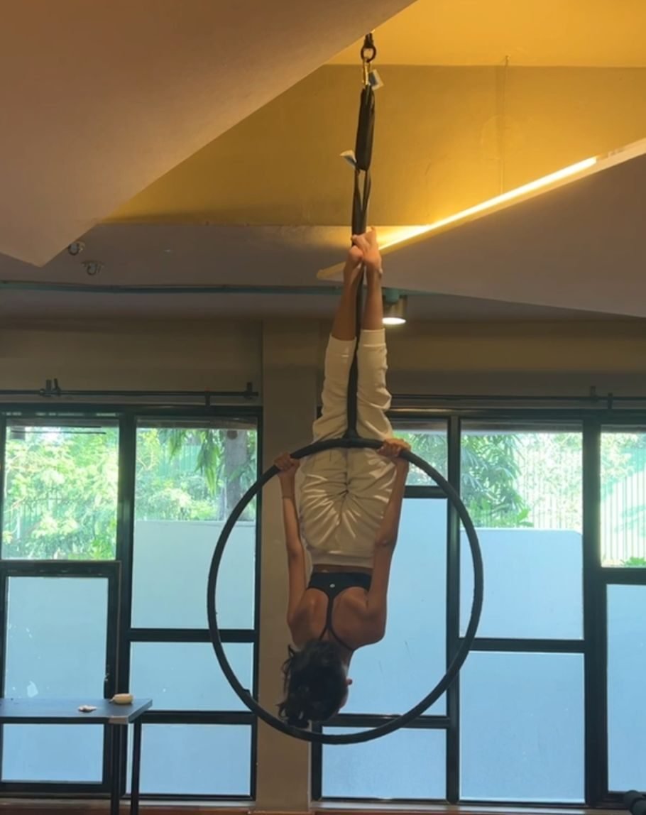 Ariana inverted on an aerial hoop, hanging by her knees