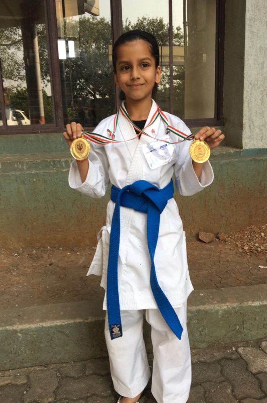 A young Ariana in a karate gi with a blue belt holding two gold medals