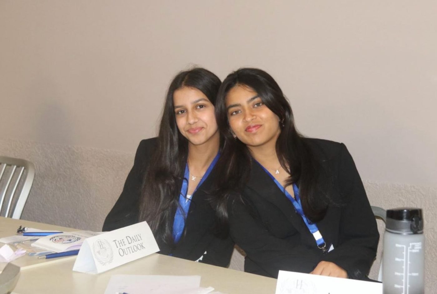 Ariana and a fellow journalist at a desk with a placard reading The Daily Outlook