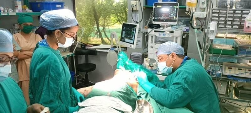 Ariana in scrubs and a surgical cap standing in an operating theatre at the National Burns Centre while a surgeon works