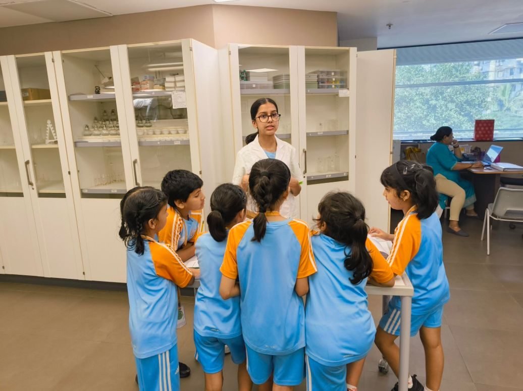 Ariana in a lab coat explaining to a cluster of children in the school laboratory