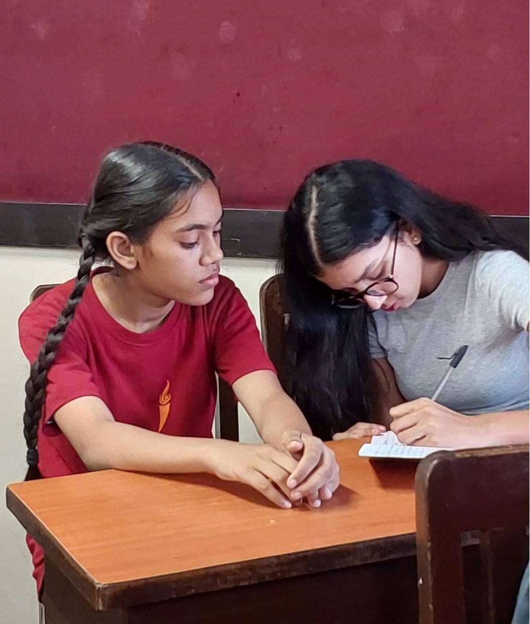 Ariana writing in a notebook beside a student at a desk