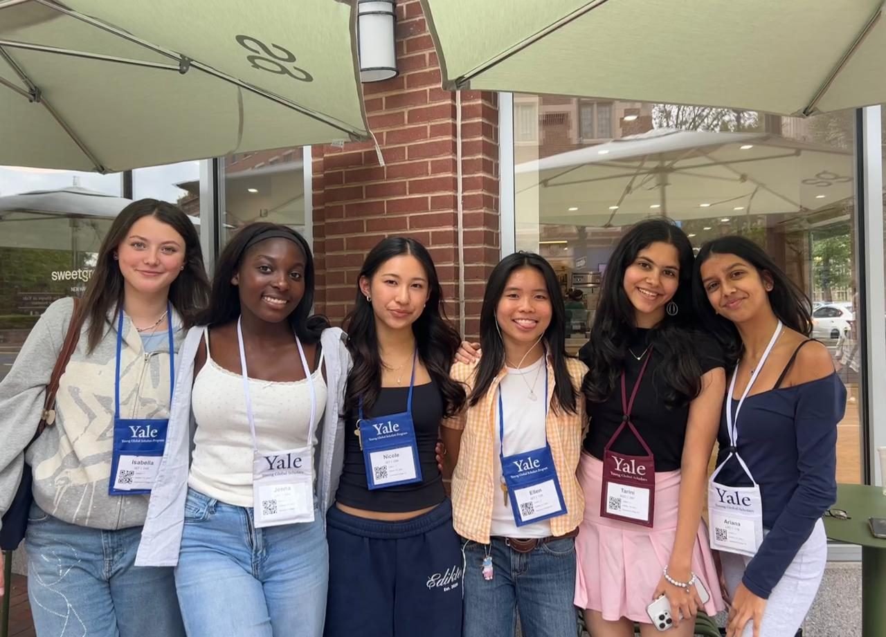 Six students wearing Yale lanyards outside a café