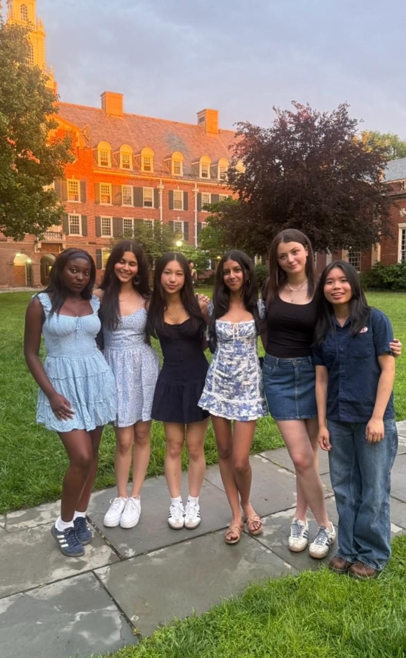 Ariana with five fellow scholars on a lawn in front of a Yale residential college at dusk